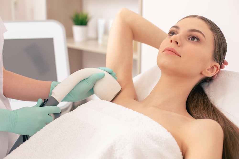 Young woman lying comfortably on a treatment bed receiving laser hair removal treatment on her underarm.